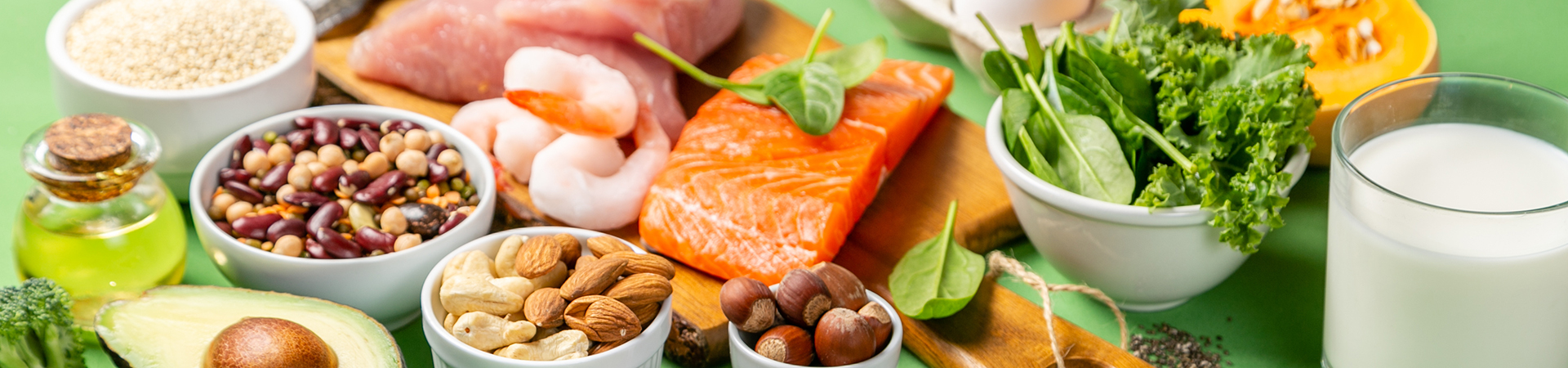 An assortment of foods featuring nuts, fish, eggs, milk, and fresh vegetables arranged on a wooden table.