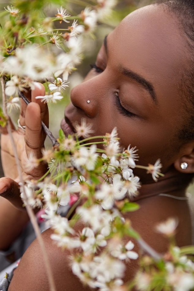 A young woman with closed eyes, smelling cherry blossoms on a tree branch in springtime, enjoying the fresh air and the beauty of nature.